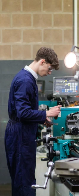 A student in navy-blue overalls operating a lathe machine in a mechanical engineering workshop, focused on precision machining. A student in navy-blue overalls operating a lathe machine in a mechanical engineering workshop, focused on precision machining.